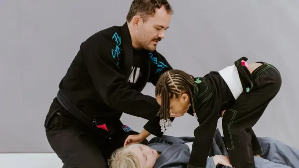 An instructor helping two young kids in kimonos learn a technique