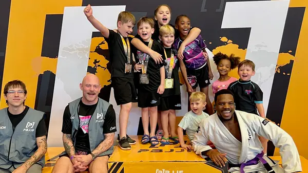 SuperFly BJJ kids competition team on the first-place podium with their medals and coaches at a PBJJF tournament