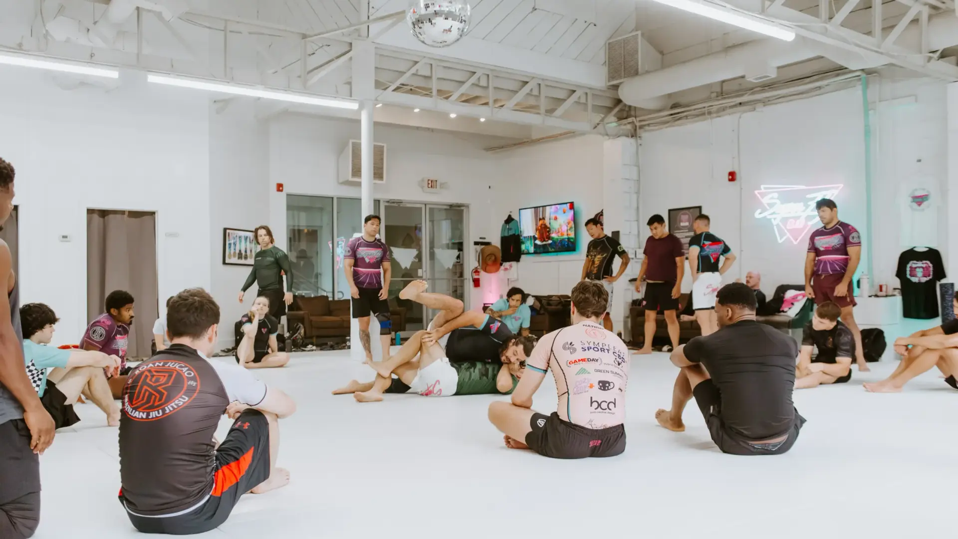 Students on the mats in SuperFly BJJ's bright training room in Decatur, with the neon SuperFly logo on the wall.
